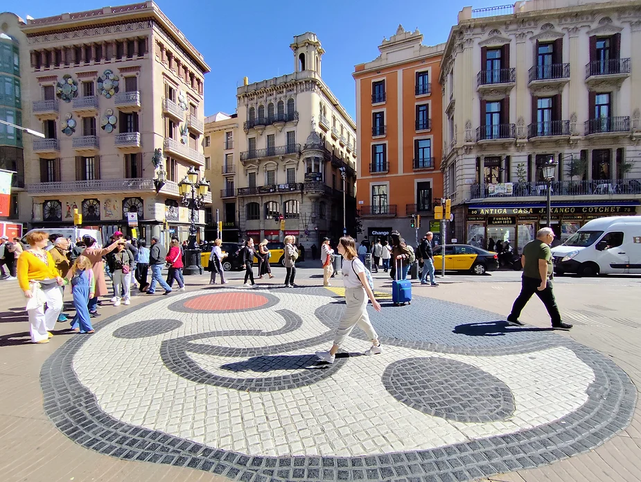 A sunny day in Barcelona, travellers walk across the Joan Miró mosaic on the floor of Las Ramblas Barcelona