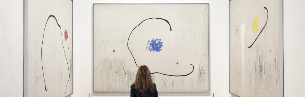 A lady contemplates a triptych of artworks by Joan Miró in the Miró museum.